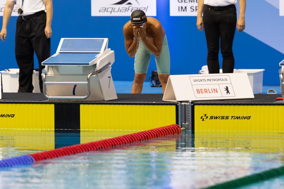 Schwimmer bereitet sich an der Startblockkante auf den Wettkampf vor, während das Wasserspiegelbild reflektiert.