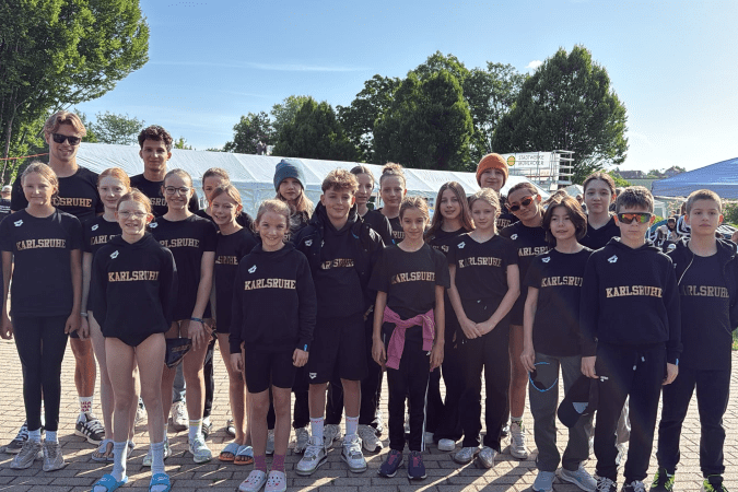 Gruppenfoto von Jugendlichen in schwarzen Trainingsanzügen mit „Karlsruhe“-Aufdruck, stehend auf einem Sportgelände.