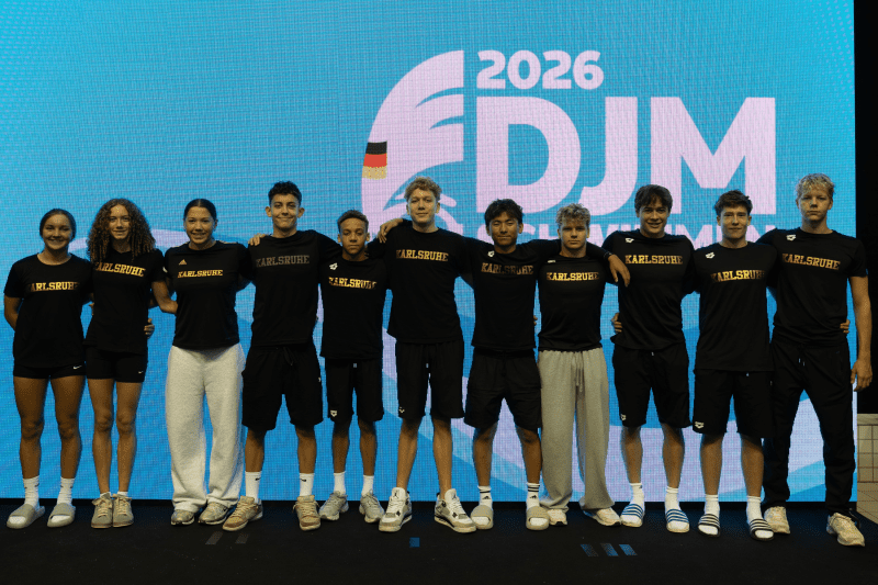 Gruppe von zehn Sportlern in schwarzen T-Shirts mit der Aufschrift "Karlsruhe" vor einem Hintergrund mit dem Logo der DJM 2026.